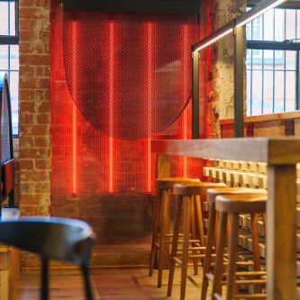 A cozy bar at Maneki Ramen in Birmingham, featuring red lights and wooden stools for a warm atmosphere.