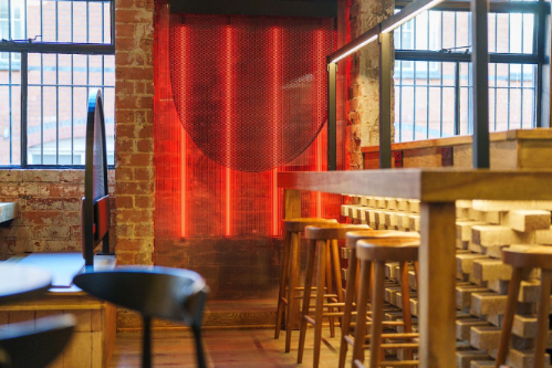 A cozy bar at Maneki Ramen in Birmingham, featuring red lights and wooden stools for a warm atmosphere.