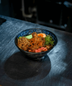 Savor Maneki Ramen’s rich and flavorful bowl featuring tender braised meat, marinated egg, pickled ginger, and fresh toppings in a deep umami broth